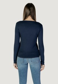 Maglione a maniche lunghe blu navy visto da dietro, con scollatura rotonda e una texture liscia. Indossato con jeans attillati blu chiaro.