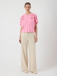 Tricou scurt din bumbac roz, cu perforații florale pe umeri, asortat cu pantaloni din in crem cu croi larg și balerini bej deschis.