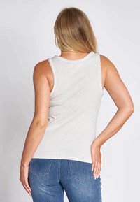 Light gray cotton tank top with a rounded neckline and thin straps, paired with blue denim jeans, showing a snug fit and casual design.