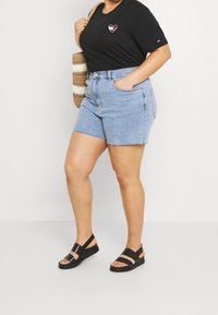 Sort T-shirt med korte ærmer og hjerte-logo, lyseblå denimshorts med frynset kant og sorte sandaler med ankelrem og flad sål.