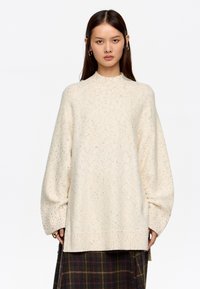 Kremowy, oversize'owy sweter z wysokim kołnierzem, teksturowany kolorowymi plamkami, z prążkowanymi mankietami i luźnym krojem.