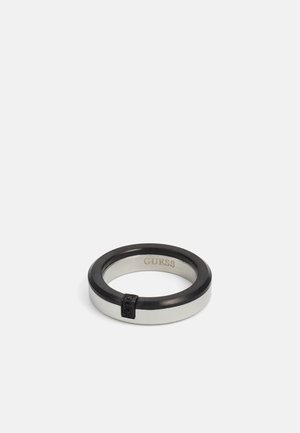 Silver and black ring with a smooth finish, featuring a thin black band and a small accent detail on the side. Engraved "GUESS" inside.