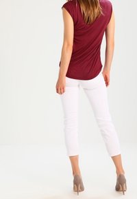 Haut bordeaux à manches courtes avec un dos drapé, associé à un pantalon blanc court et des talons hauts beiges texturés.