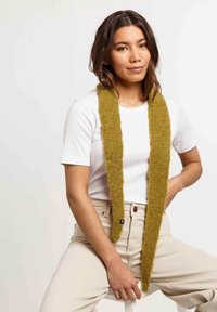 Écharpe en vert olive, texturée, en matériau doux, portée sur un t-shirt blanc, avec une forme rectangulaire slim et un design minimaliste.