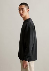 Schwarzes Langarmshirt aus weichem Stoff, mit lockerem Schnitt, Rundhalsausschnitt und seitlichen Schlitzen, kombiniert mit gestreiften Hosen.