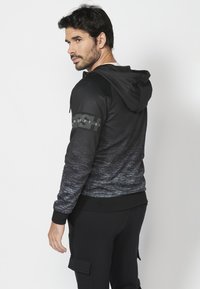 Čierna mikina s kapucňou a ombré textúrou prechádzajúcou do šedej, obsahuje kapucňu, rebrované manžety a označenie značky na rukáve.