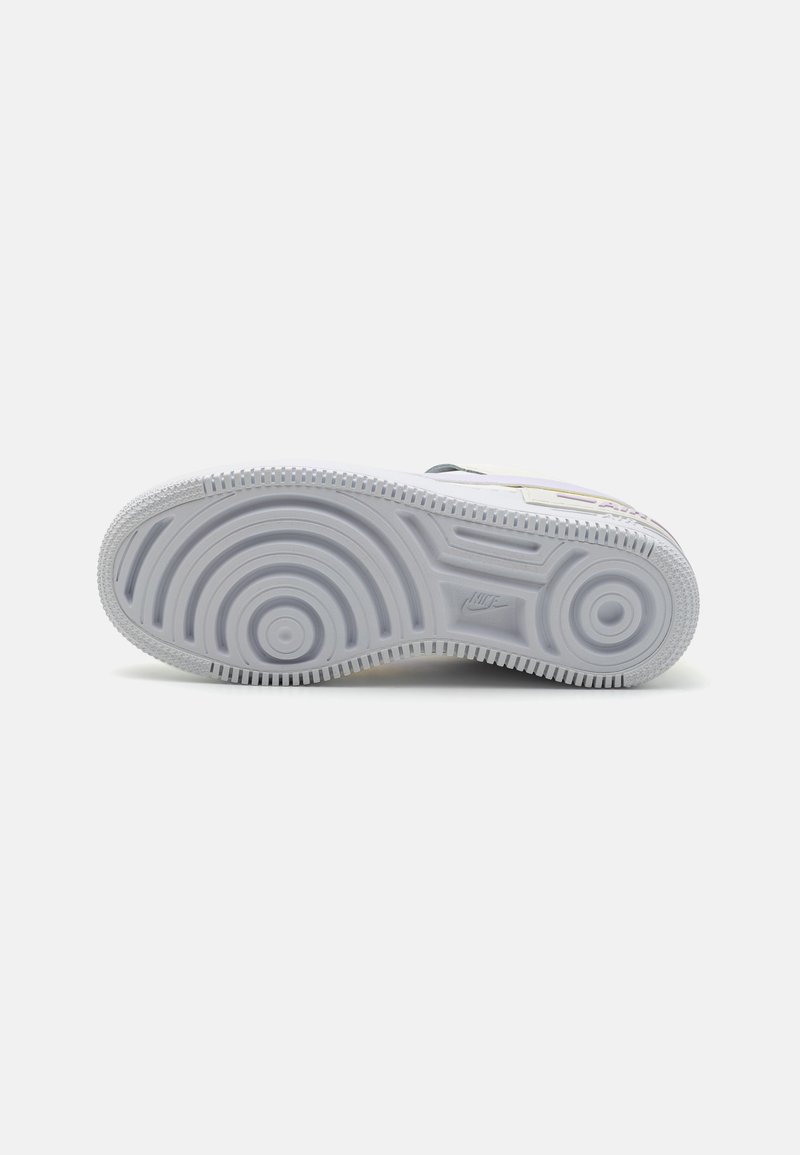 Suela de zapatilla blanca con patrones texturizados y diseños circulares. Presenta una entresuela gris y una suela exterior de goma ligeramente veteada.