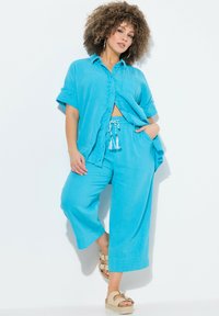Ensemble léger en turquoise composé d'une chemise courte à boutons et d'un pantalon large avec une taille à cordon de serrage et des accents de pompons.
