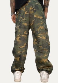 Pantaloni cargo con motivo mimetico, dotati di molteplici tasche, vestibilità ampia e tessuto strutturato. Indossati con sneakers bianche.