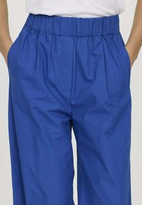 Pantalons en coton bleu avec une taille élastique, dotés de poches latérales et d'une coupe décontractée, présentant une texture lisse et un design léger.