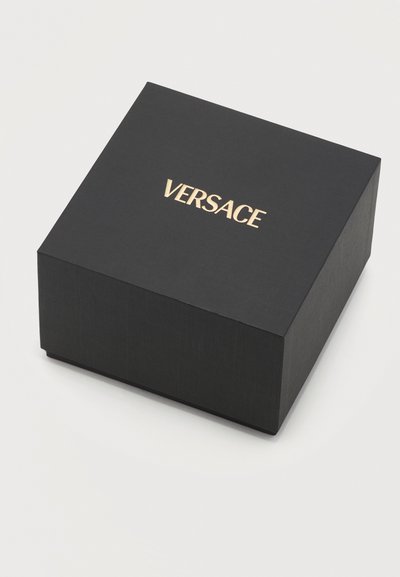 Čierna štvorcová krabička s textúrovaným povrchom a zlatým logom „VERSACE“ umiestneným v strede veka, na jednoduchom svetlom pozadí.