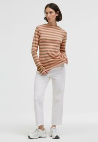 Long-sleeve striped top in soft pink and taupe, made from a lightweight fabric. Paired with white straight-leg jeans and sneakers.