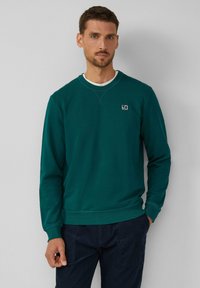 Sudadera verde en una mezcla de algodón, con cuello redondo, puños acanalados y un pequeño logo en el pecho. Ajuste casual y textura suave.
