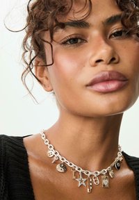 Collana in argento con diversi ciondoli, tra cui un simbolo di pace, una stella e bottoni, con accenti neri e dorati.