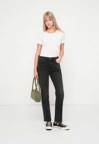 Jean noir taille haute, coupe slim, associé à un haut blanc à manches courtes. Les accessoires comprennent un sac à main vert et des baskets noires.