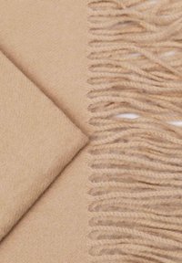 Sciarpa di lana beige con una consistenza morbida, piegata ordinatamente con un bordo frangiato. Le fibre sono leggermente pelose, aggiungendo calore e dettaglio.