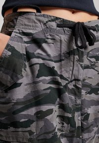 Persoon in grijs en zwart camouflage shorts met een zwarte koordsluiting, en een deel van een zwart shirt zichtbaar boven de taille.