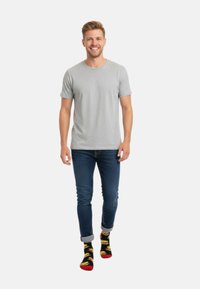 Grå bomullströja, blå denimjeans och svarta strumpor med hamburgermönster. Modell som går och visar en avslappnad outfit.