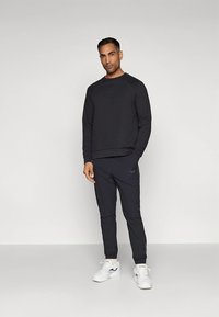 Zwarte sweatshirt met geribbelde manchetten, gecombineerd met bijpassende zwarte taps toelopende joggers. Voorzien van een subtiel logo en witte sneakers.