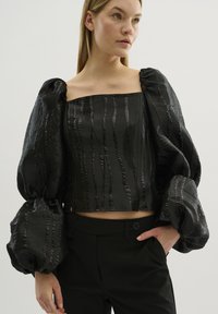 Zwarte cropped top met oversized, textuurvolle ballonmouwen, voorzien van verticale strepen, een vierkante halslijn en een gladde satijnen afwerking.