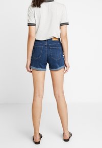 Džínové šortky s ohrnutými lemy, tmavé praní, pět kapes a kožená nášivka na pase; kombinované se šedým žebrovaným tričkem.