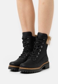 Botas de cuero negro con cordones, que cuentan con un cuello de piel sintética, un acabado texturizado y una suela de goma robusta con un borde marrón contrastante.