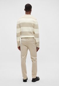 Beige ja kreemikäärõngastega sviiter ribide tekstuuriga, koos heledate beežide pükste ja mustade kingadega. Nähtavad selja detailid ja õmblused.