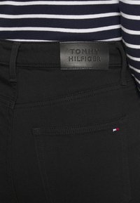 Dettaglio di jeans neri Tommy Hilfiger con tasca posteriore cucita e etichetta in pelle sopra la vita.