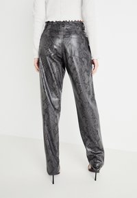 Schlangenmuster-Hosen aus einem glänzenden, strukturierten Stoff; mit hoher Taille und frilliertem Saum, lockerer Passform und mit Gesäßtaschen versehen.