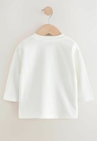 Chemise blanche en coton à manches longues avec un col rond et des épaules tombantes, dotée d'une finition sans couture et d'un petit logo imprimé au dos du col.