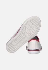 Zapatillas de lona con una parte superior blanca sólida, acentos rojos y una suela de goma texturizada con un diseño a rayas.