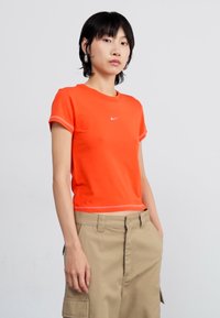 Narancssárga, rövid fazonú póló, puha anyagból készült, körkivágással és rövid ujjal. Kiemelkedő, fehér Nike logó a mellkason.