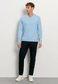 Hellblaues V-Ausschnitt-Sweatshirt aus weichem Material, kombiniert mit schwarzen Hosen und weißen Sneakers, in einem schlanken Fit-Design.