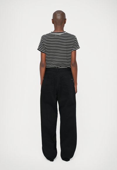 Gestreiftes Schwarz-Weiß-T-Shirt mit kurzen Ärmeln, kombiniert mit locker sitzenden schwarzen Hosen mit hoher Taille und zwei Gesäßtaschen.