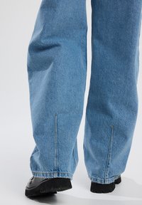 Lichtblauwe denim wijde broek met een schone afwerking, voorzien van zijopeningen en gestikte naden, gecombineerd met zwarte schoenen met een dikke zool.