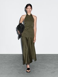 Robe sans manches vert olive avec fermeture à boutons et col haut, associée à une pochette noire texturée et des sandales à lanières noires.