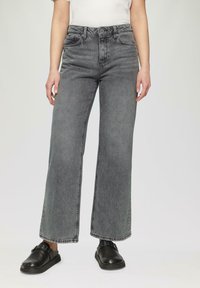 Hoch geschnittene, weit geschnittene Jeans aus verwaschenem schwarzem Denim. Verfügt über fünf Taschen, Gürtelschlaufen und gestickte Details an den Nähten. Kombiniert mit schwarzem Schuhwerk.