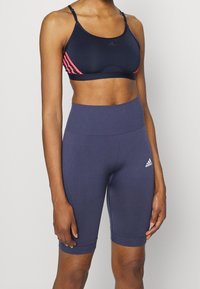 Granatowy sportowy biustonosz z różowymi paskami i regulowanymi ramiączkami, zestawiony z granatowymi szortami rowerowymi z wysokim stanem, ozdobionymi logo i wykonanymi z gładkiego, elastycznego materiału.