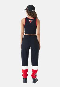 Top corto nero con accenti rossi e logo di un toro, abbinato a pantaloni della tuta neri con strisce rosse e bianche sui polsini. Sneakers nere.