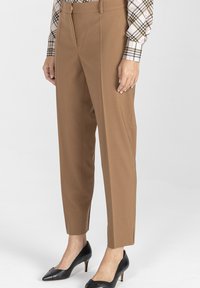 Dopasowane brązowe spodnie o gładkiej fakturze, zwężanym kroju i bocznych kieszeniach, połączone z czarnymi szpilkami w spiczastym kształcie.