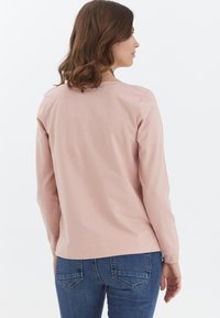 Camiseta de algodón rosa de manga larga con escote redondo, corte relajado y detalles de costura sutiles, combinada con unos pantalones vaqueros azul denim.