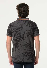 Zwarte polo shirt met groot bladerenpatroon, korte mouwen en een kraag. Heeft oranje accenten langs de kraag en de mouwzoom.