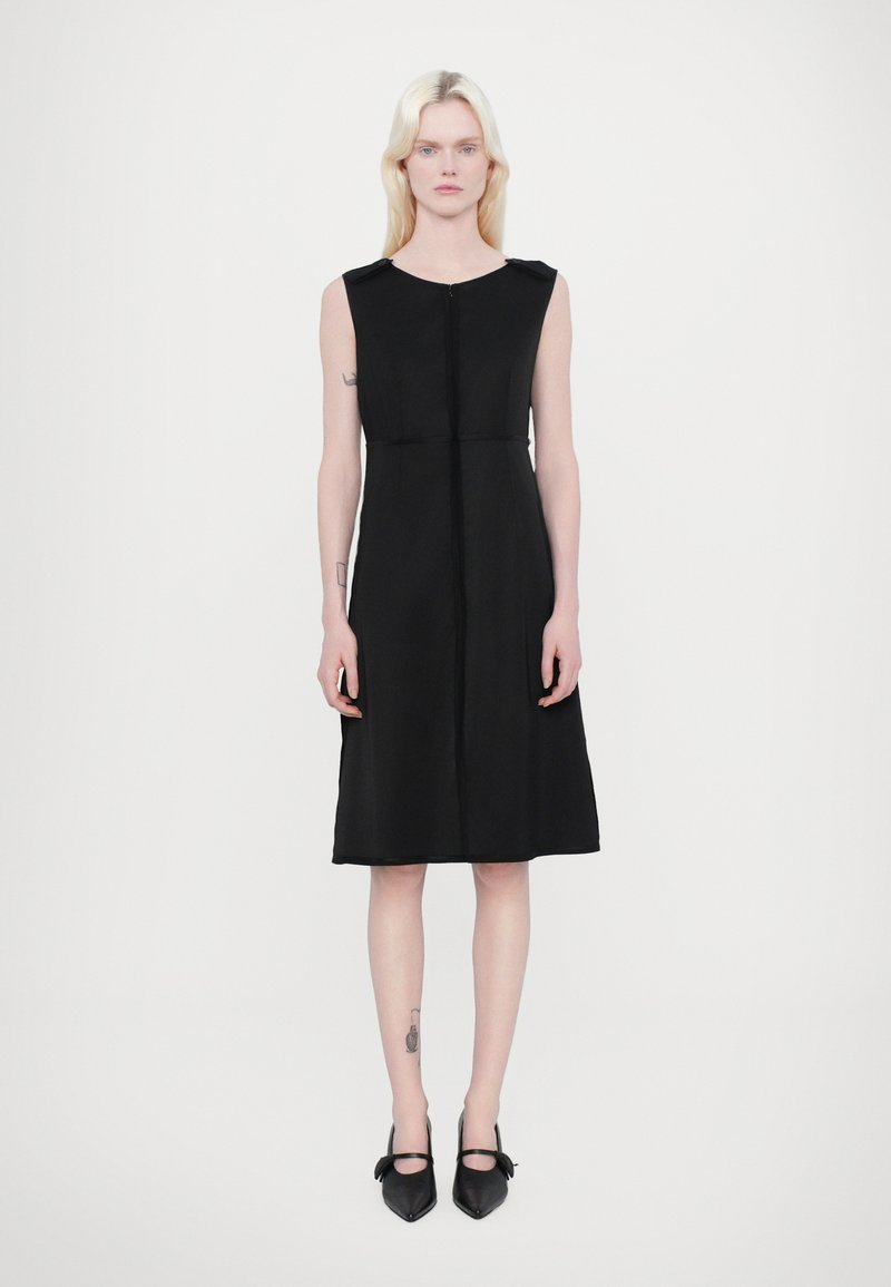 Robe noire sans manches avec fermeture éclair et taille cintrée. Tissu lisse et léger ; longueur au genou avec une légère silhouette en A.