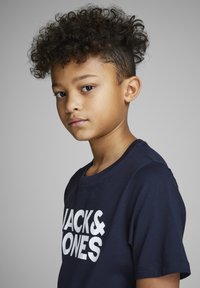 Modra bombažna majica s kratkimi rokavi, bele barve z napisom "JACK & JONES", zaobljen izrez in sproščen kroj. Gladka tekstura.