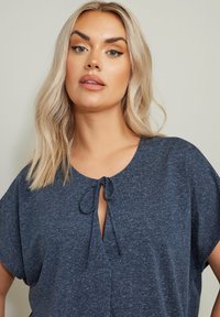 Top blu navy a maniche corte in morbido tessuto testurizzato, con scollatura rotonda e dettaglio con nodo sul davanti, dalla vestibilità rilassata.