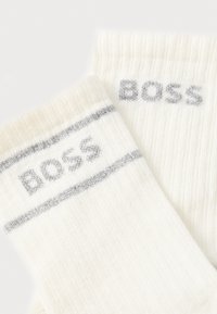 Calzini bianchi a coste con una striscia argentata e la parola "BOSS" in lettere argentate. Texture morbida con una vestibilità aderente.