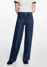 Široke jeans hlače iz temno modrega jeansa, z kontrastnim šivanjem, visokim pasom in dvema zadnjima žepoma. Ujemanje z črnimi platform čevlji.