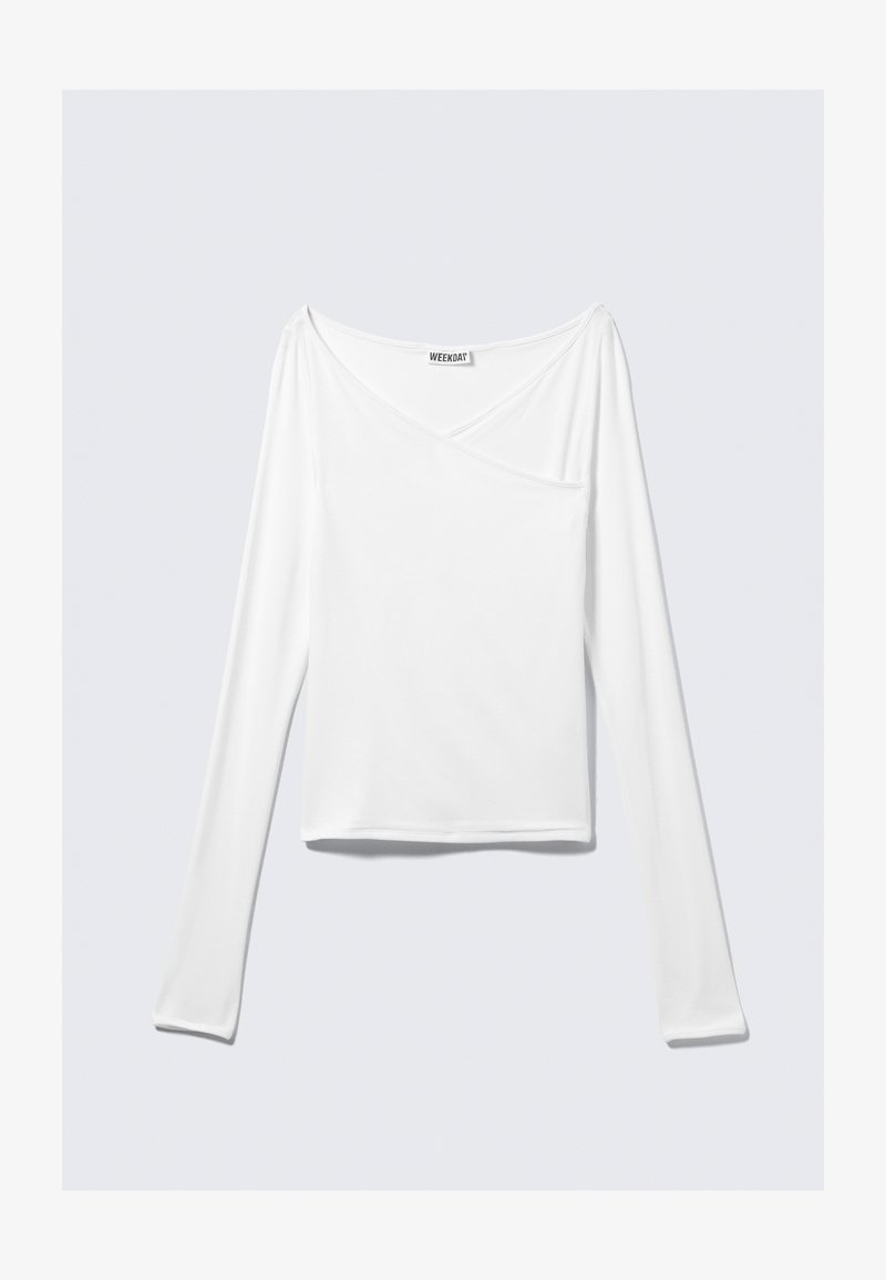 Haut blanc à manches longues avec un design croisé et une poche. Fabriqué dans un tissu lisse et extensible. Coupé dans une coupe décontractée et ample.