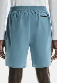 Pantalones de baño ligeros y azules con una cintura elástica, bolsillos laterales y un bolsillo trasero con cremallera. Textura suave con un ajuste estándar.
