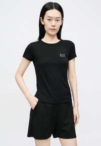 Mustast suletähelisest kangast lühikeste varrukatega t-särk, vasakul rinnal väike EA7 logo. Sobitatuna mustade lühikestega.